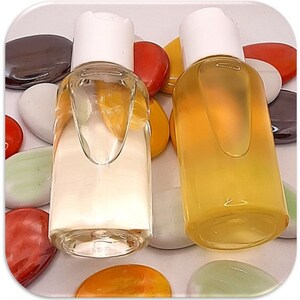 May include: Two clear glass bottles with white caps filled with a light yellow liquid. The bottles are sitting on a white surface with colorful stones.