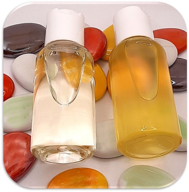 May include: Two clear glass bottles with white caps filled with a light yellow liquid. The bottles are sitting on a white surface with colorful stones.