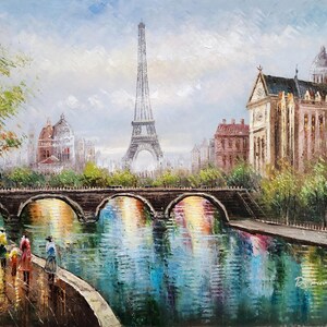 May include: Oil painting of Paris featuring the Eiffel Tower, a bridge, and buildings along a river. The artwork uses a palette of blues, greens, and browns, with reflections in the water. Figures stroll along the riverbank, adding a sense of scale.