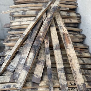 May include: A stack of reclaimed wood planks, likely from old barrels, with a weathered and rustic appearance. The planks are arranged in a fan shape, showcasing their natural grain and dark brown colour.