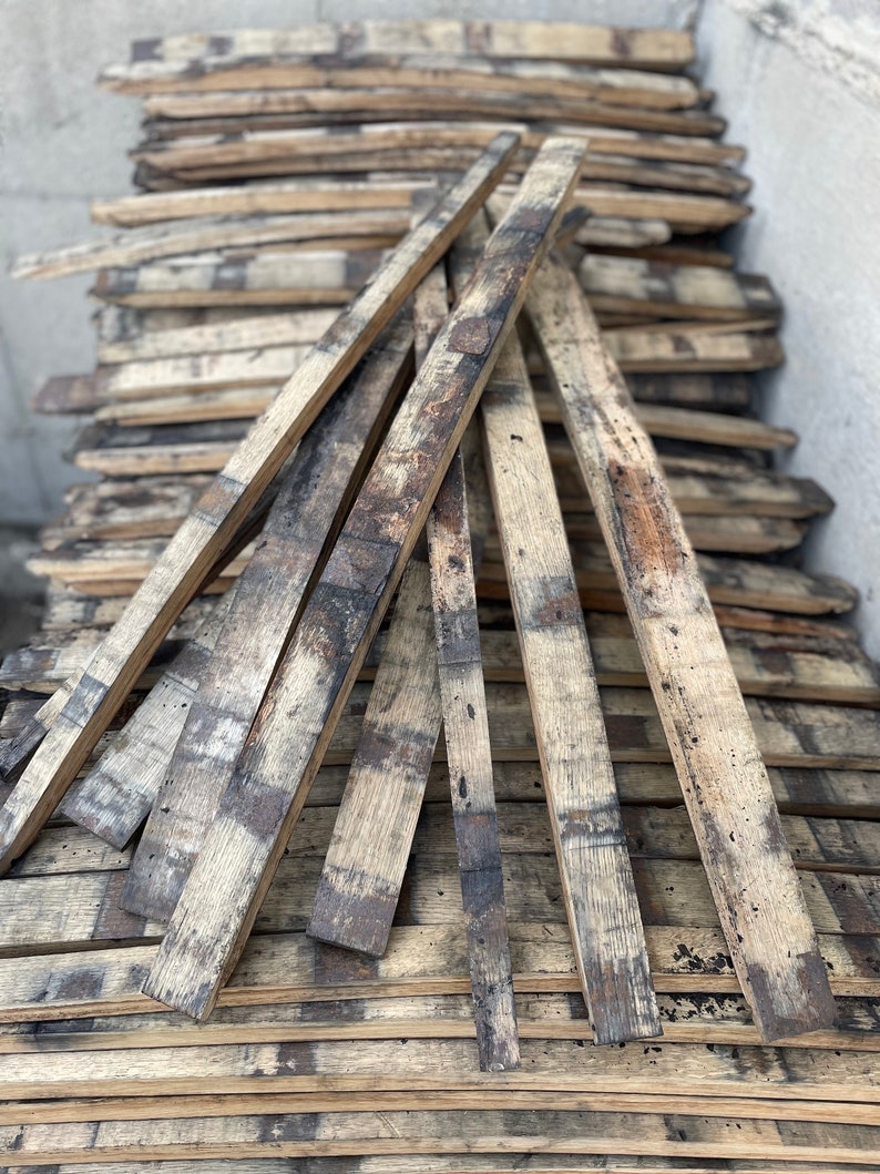 May include: A stack of reclaimed wood planks, likely from old barrels, with a weathered and rustic appearance. The planks are arranged in a fan shape, showcasing their natural grain and dark brown colour.