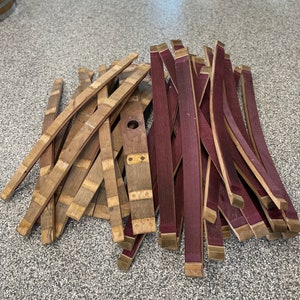 May include: A pile of wooden barrel staves, some are natural wood colour and some are stained a deep purple.