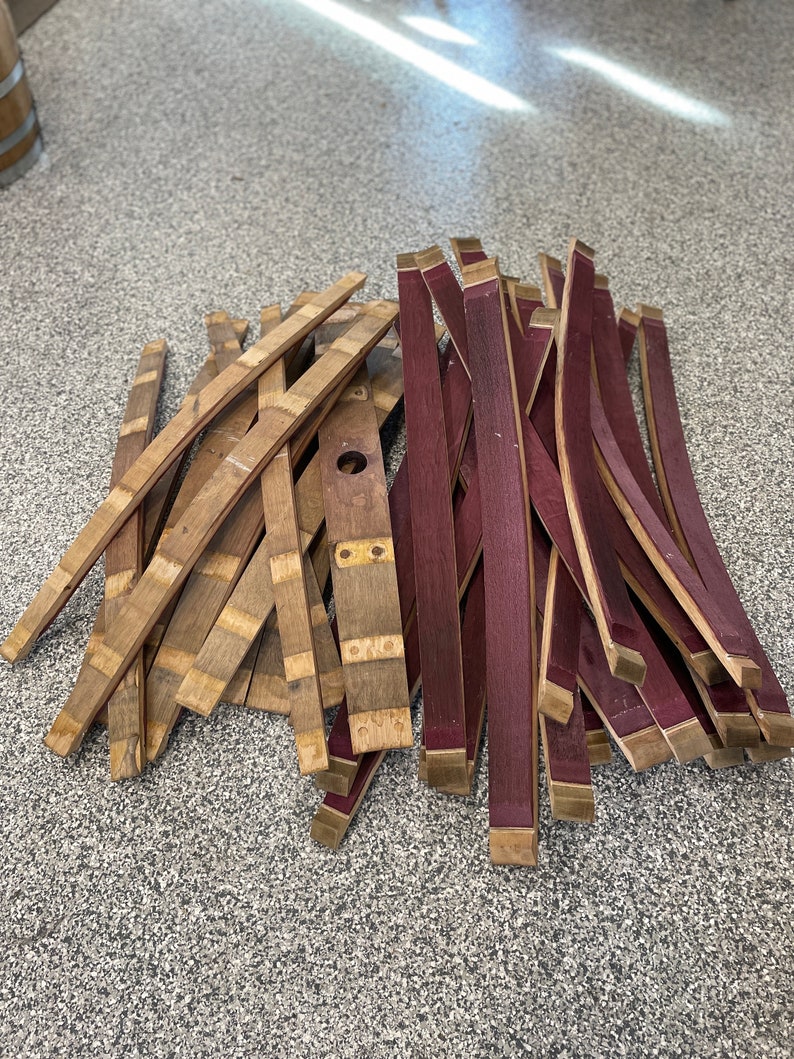 May include: A pile of wooden barrel staves, some are natural wood colour and some are stained a deep purple.