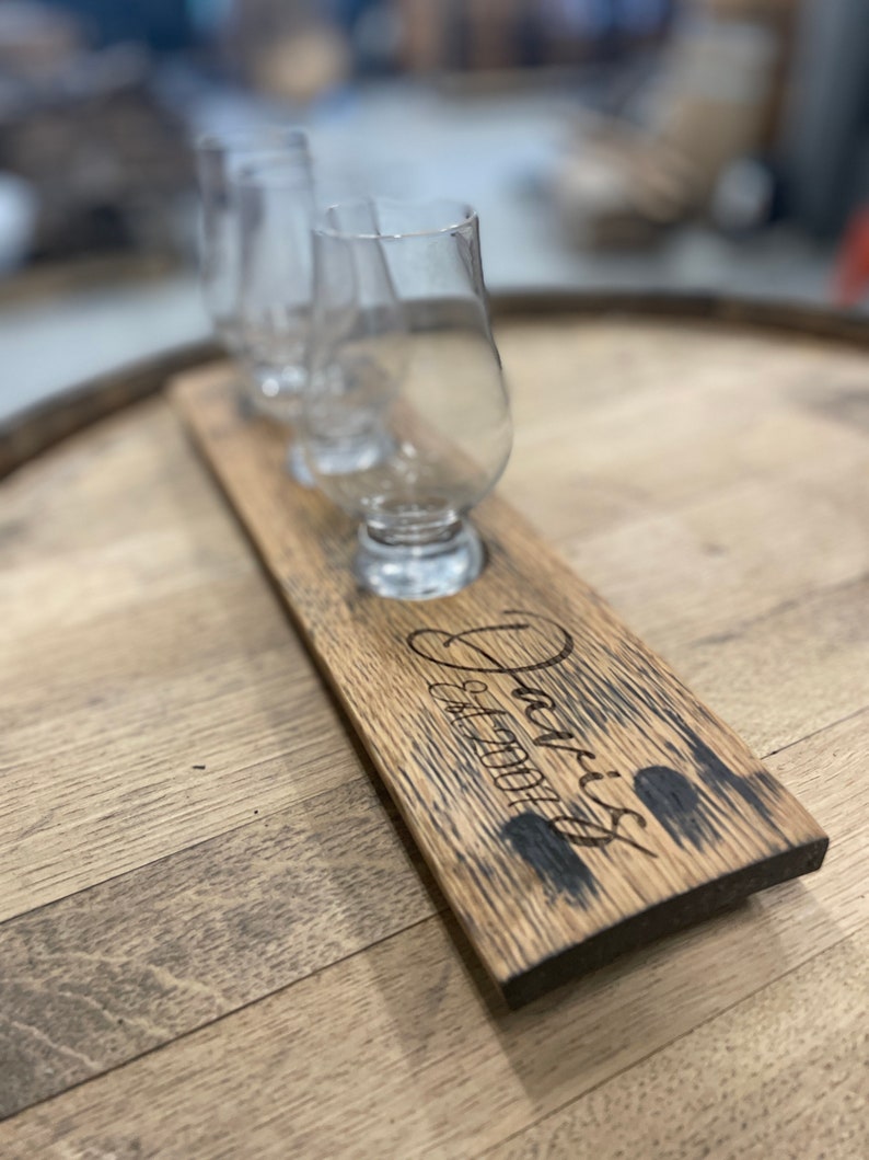 Może przedstawiać: Drewniana taca do degustacji whisky z trzema szklankami i napisem "Jack's Est. 2001".