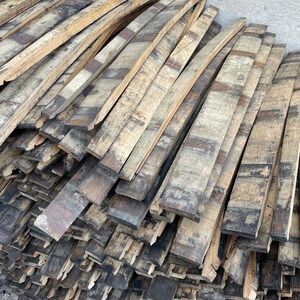 May include: A stack of reclaimed wood planks from old whiskey barrels. The wood is a mix of light and dark brown with black char marks. The planks are stacked in a staggered pattern.