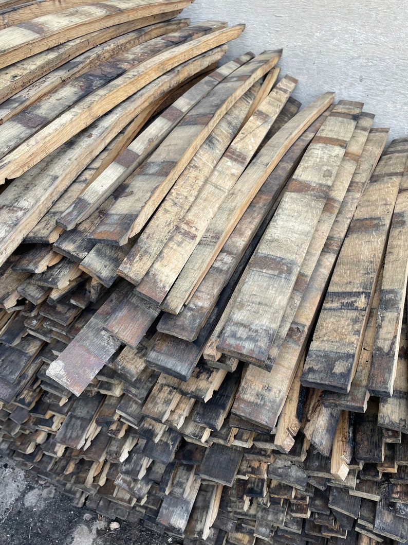 May include: A stack of reclaimed wood planks from old whiskey barrels. The wood is a mix of light and dark brown with black char marks. The planks are stacked in a staggered pattern.