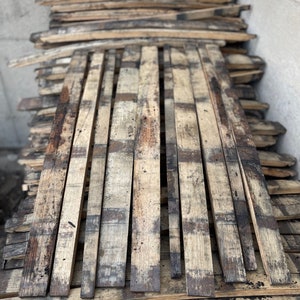 May include: A stack of reclaimed wood planks, probably from old barrels, with a weathered, rustic appearance. The planks are arranged in a staggered pattern, showing their natural grain and texture.