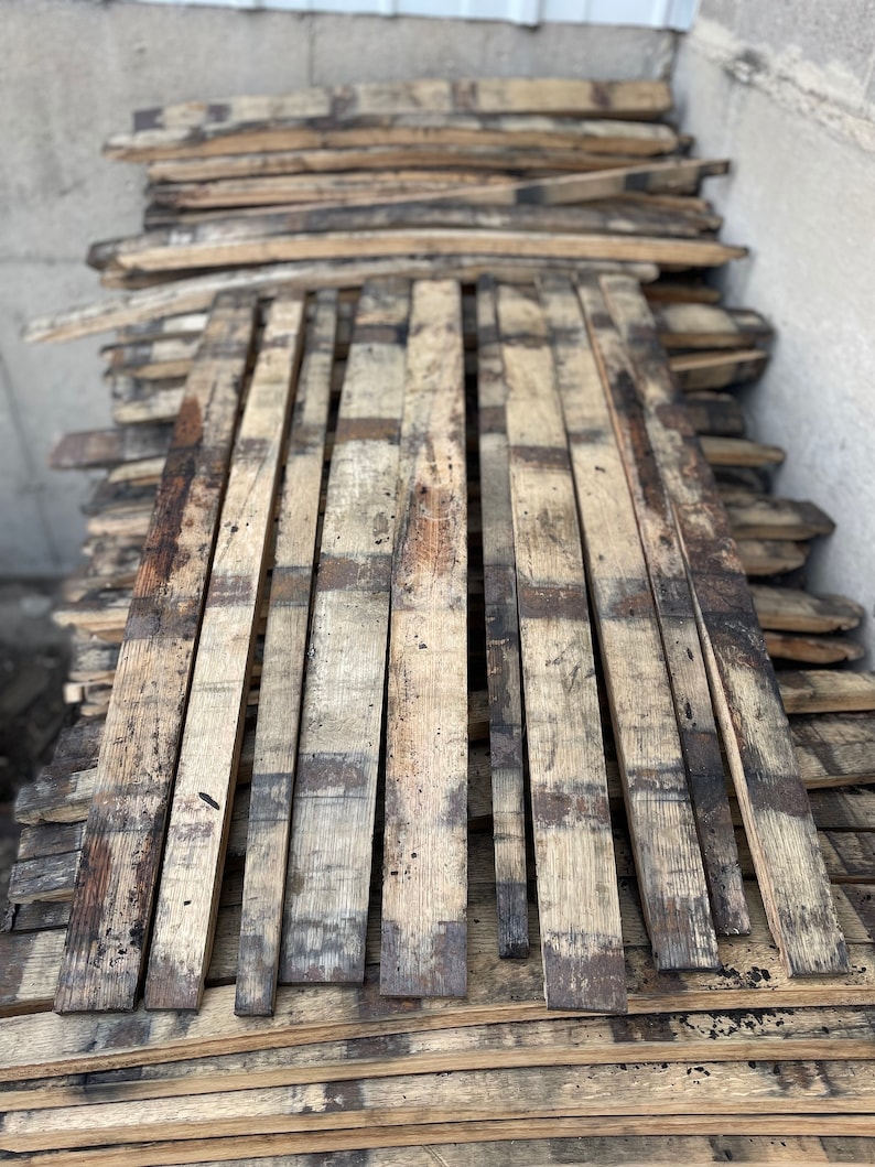 May include: A stack of reclaimed wood planks, probably from old barrels, with a weathered, rustic appearance. The planks are arranged in a staggered pattern, showing their natural grain and texture.