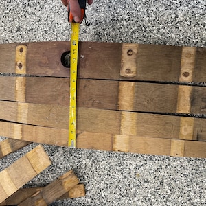 May include: A set of wooden barrel staves, measuring 76 cm in length, arranged in a row on a grey surface. The staves are made of light brown wood with darker brown accents. A yellow measuring tape is placed next to the staves.