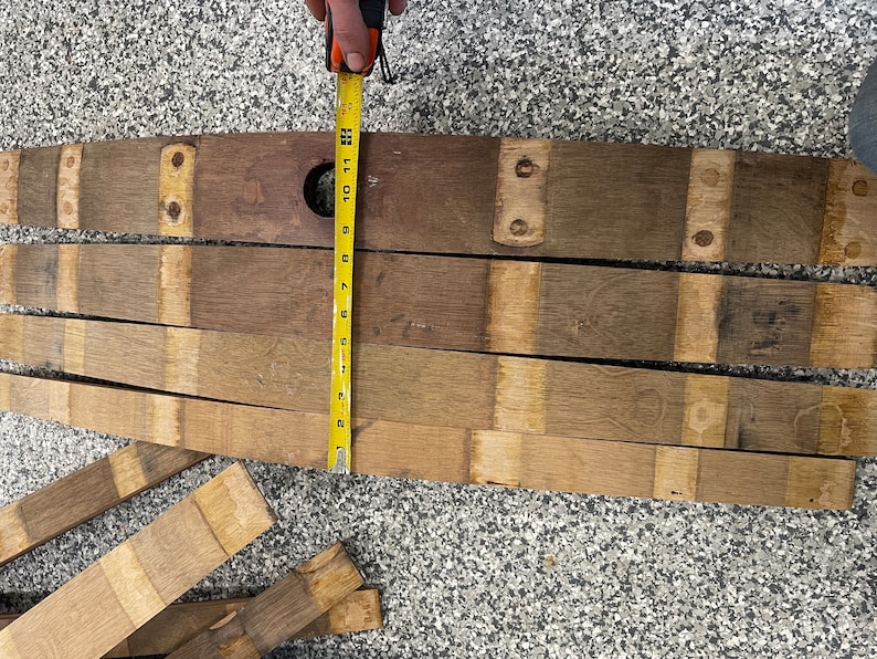 May include: A set of wooden barrel staves, measuring 76 cm in length, arranged in a row on a grey surface. The staves are made of light brown wood with darker brown accents. A yellow measuring tape is placed next to the staves.