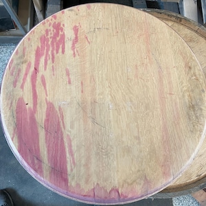 May include: A close-up of a round wooden barrel top with a reddish-brown stain. The wood is light brown and has a natural grain pattern.