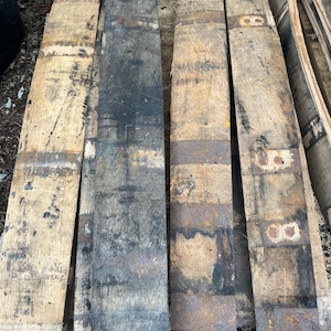 May include: Four reclaimed wooden barrel staves, showcasing a rustic aesthetic. The staves vary in color, from light tan to dark charcoal, with visible grain and metal bands. These pieces are ideal for woodworking projects or adding a vintage touch to decor.