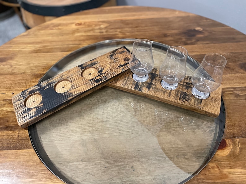 Może przedstawiać: Trzy przezroczyste szklanki do degustacji whisky stoją na drewnianej tacy z trzema wgłębieniami. Taca wykonana jest z odzyskanego drewna i ma ciemnobrązowe zabarwienie. Taca stoi na drewnianym stole.