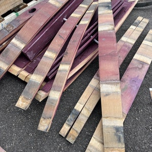 May include: A pile of reclaimed wine barrel staves, some are stained a deep purple, others are natural wood colour. The staves are arranged in a random pattern, some are curved, others are straight. The staves are all about 2.5 cm wide and 90 cm long.