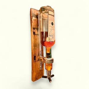 May include: A wall-mounted liquor dispenser made from reclaimed wood with a clear glass bottle and a metal spout. The bottle is filled with amber-colored liquid.