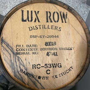 K&ouml;nnte beinhalten: Ein Holzfass mit schwarzer Beschriftung, die "LUX ROW DISTILLERS DSP-KY-20044 FILL DATE: 20013 CONTENTS BOURBON WHISKEY SERIAL NO: 47141 RC-53WG C BARDSTOWN KENTUCKY" lautet.