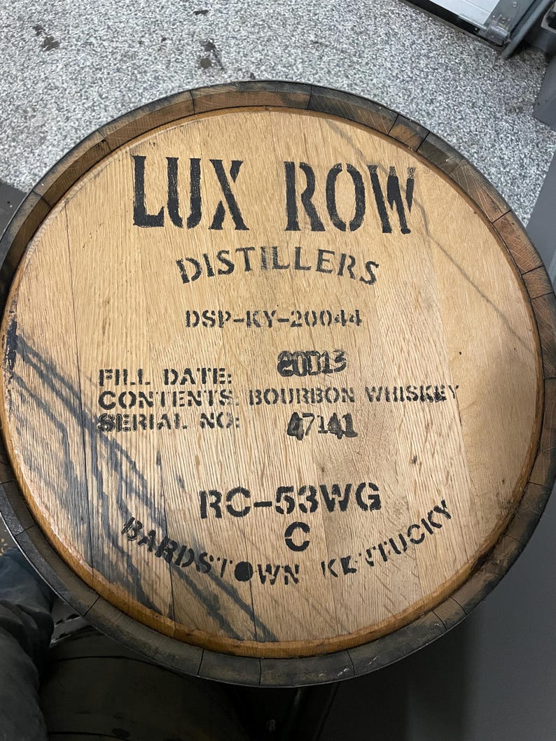 K&ouml;nnte beinhalten: Ein Holzfass mit schwarzer Beschriftung, die "LUX ROW DISTILLERS DSP-KY-20044 FILL DATE: 20013 CONTENTS BOURBON WHISKEY SERIAL NO: 47141 RC-53WG C BARDSTOWN KENTUCKY" lautet.