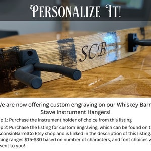 May include: A wooden whiskey barrel stave instrument hanger with two black guitar hooks. The hanger is personalized with the initials "SCB".