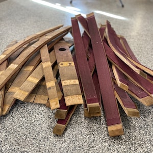 May include: A pile of wooden barrel staves, some are natural wood colour and some are stained a deep burgundy red.