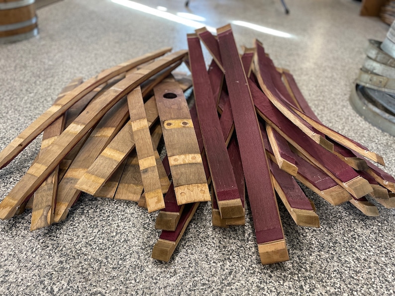 May include: A pile of wooden barrel staves, some are natural wood colour and some are stained a deep burgundy red.
