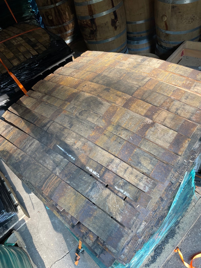 May include: A stack of reclaimed wooden barrel staves, showing the aged, weathered appearance of the wood. The staves are held together with metal bands, and are ready for reuse in woodworking projects. The wood has a mix of brown and gray tones.