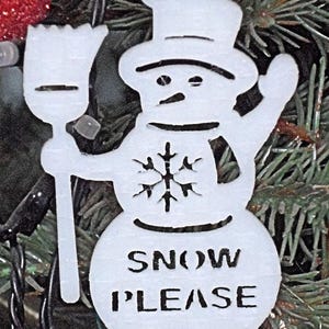 May include: White snowman ornament with a black hat, a snowflake design, and the words "SNOW PLEASE" on the front.