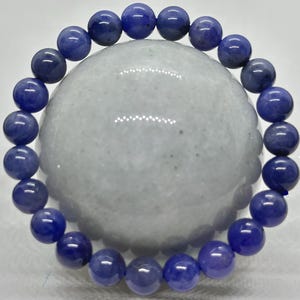 Può includere: Un braccialetto elastico circolare composto da perline sferiche lisce e levigate in varie tonalità di blu reale profondo e viola. Le perline presentano variazioni di colore naturali e sottili texture interne disposte in un cerchio.