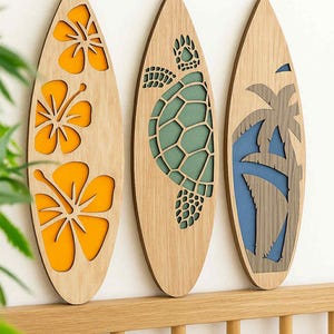 May include: Three wooden surfboard-shaped wall decorations. One features orange hibiscus flowers, another a green turtle, and the last a blue and gray palm tree. The surfboards are mounted on a light-colored wooden rail.
