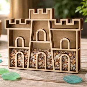May include: A wooden castle-shaped display shelf filled with seashells and small stones. The castle has arched openings and a crenelated top. Colorful glass stones are scattered around the base of the castle.