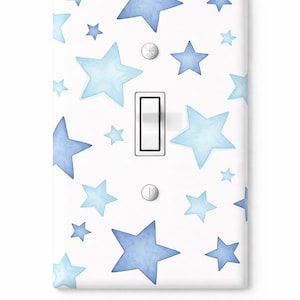 Puede incluir: Cubierta de interruptor de luz blanca decorada con estrellas azules de estilo acuarela de varios tamaños. El interruptor tiene una palanca blanca y dos tornillos plateados. El diseño es de temática celestial.