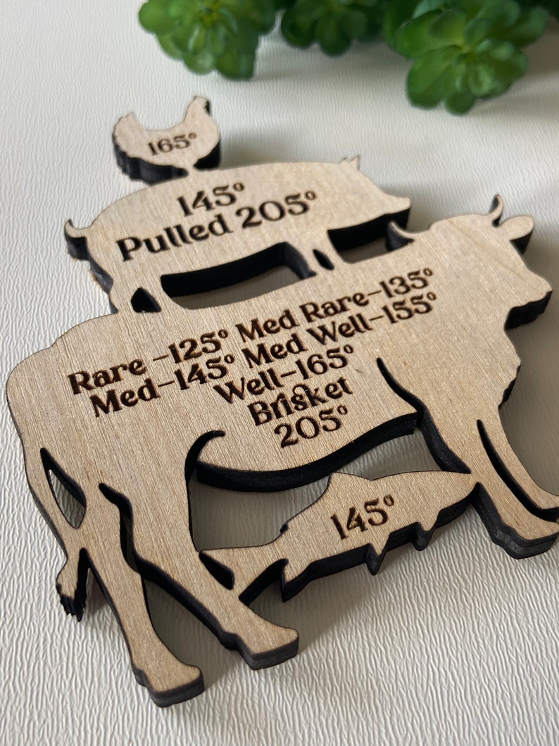 May include: Wooden food temperature guide with cut-out shapes of a chicken, pig, cow, and fish. The guide includes temperatures for cooking various meats, such as pulled pork at 205 degrees Fahrenheit and brisket at 205 degrees Fahrenheit.