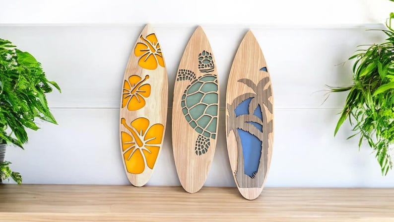 May include: Three wooden surfboards with decorative cutouts. One features yellow hibiscus flowers, another a teal turtle, and the last a palm tree with a blue background. The surfboards are displayed against a white wall.