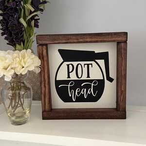 May include: A wooden sign with a black and white coffee pot graphic and the text "POT head".
