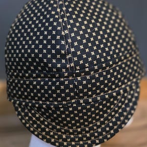 May include: A navy blue cap with a repeating pattern of small, tan four-pointed stars. The cap has a curved brim and is made of a durable fabric. The cap is designed to fit snugly on the head.