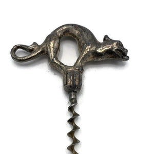 Op de afbeelding: Een zilverkleurige metalen kurkentrekker met een gedetailleerd kattenontwerp op het handvat. De kat is opgerold met zijn staart om zijn lichaam gewikkeld, en zijn kop is naar de zijkant gedraaid. De kurkentrekker heeft een lange, spiraalvormige schacht.