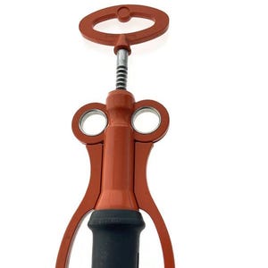 Può includere: Un cavatappi rosso e nero con un manico e due aperture circolari. Il cavatappi ha una vite metallica a spirale e una base nera. Il design è semplice e funzionale, adatto per aprire bottiglie di vino.