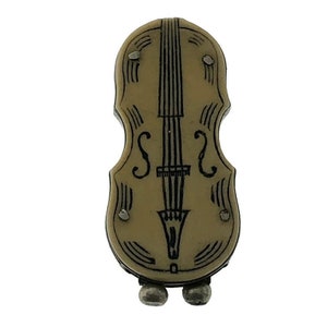 Puede incluir: Un compacto vintage de metal de color crema en forma de violín con detalles pintados en negro. El compacto tiene dos pequeños pies redondos de color plateado.