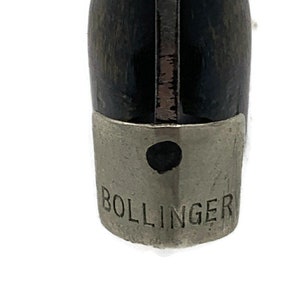 Puede incluir: Primer plano de un tapón de botella negro y plateado con la palabra "BOLLINGER" grabada en la tapa plateada.