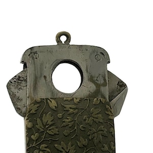 Puede incluir: Un cortapuros de plata con una cubierta de patrón floral. El cortapuros tiene un agujero redondo para cortar puros.