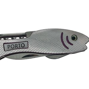 Könnte beinhalten: Silbernes Fisch-Multitool mit strukturierter Oberfläche. Mit Schlüsselring, Schraubendreher und kleiner Klinge. Das Wort "PORTO" ist auf einem rechteckigen Etikett aufgedruckt. Der Fisch hat lila Akzente für Auge und Kiemen.