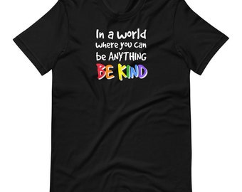 Puede incluir: Camiseta negra con el texto "En un mundo donde puedes ser cualquier cosa, SE AMABLE" en colores arcoíris.