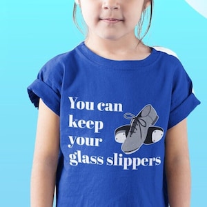 May include: A royal blue t-shirt with the text "You can keep your glass slippers" in white lettering. The shirt features a pair of gray tap shoes with black soles.