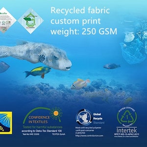 以下が含まれることがあります： カスタムプリントされた青と緑のリサイクルファブリック。ファブリックは250 GSMで、グローバルリサイクルスタンダードとインターテックの認証を受けています。画像には、海を泳ぐフグも写っています。