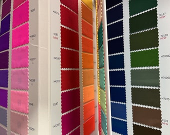 May include: A fabric swatch book featuring a range of colours, including pink, red, orange, green, blue, and brown. The swatches are labelled with numbers and some have the word "NEW" printed on them.