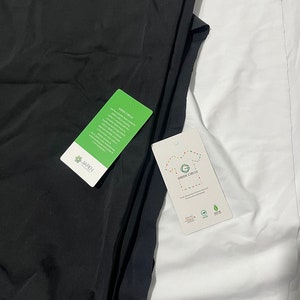 May include: Two black t-shirts with a green circle tag that says "GREEN CIRCLE" and "Pure Recycled Cotton" and a white t-shirt with a green circle tag that says "GREEN CIRCLE" and "Pure Recycled Cotton" with icons for recycled materials, organic cotton, and biodegradable.