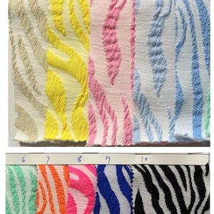 May include: Fabric swatches with a 3D leopard stripe design in various colours, including beige, yellow, pink, blue, green, orange, and black and white. The text indicates the fabric is suitable for clothes, skirts, dresses, and swimwear. The fabric width is 145cm.
