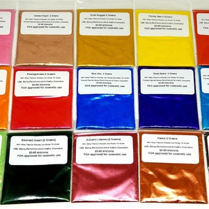 May include: A collection of 15 small, clear plastic bags filled with colorful cosmetic-grade powders. The powders are in various shades, including pink, peach, gold, yellow, red, orange, blue, green, and brown. Each bag has a white label with black text.