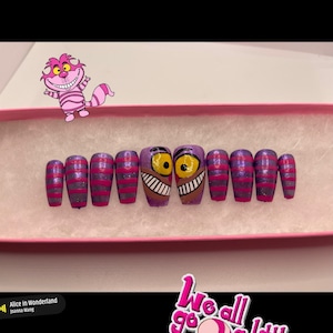 K&ouml;nnte beinhalten: Ein Set aus aufklebbaren N&auml;geln mit einem lila-rosa gestreiften Design, wobei zwei N&auml;gel das Gesicht der Grinsekatze aus Alice im Wunderland zeigen. Die N&auml;gel befinden sich in einer rosa Schachtel, mit einem Aufkleber mit der Aufschrift "We all go a little mad sometimes."