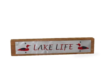 May include: A wooden sign with a metal plaque that reads "LAKE LIFE" in black script. The plaque is decorated with two red and black loon silhouettes.