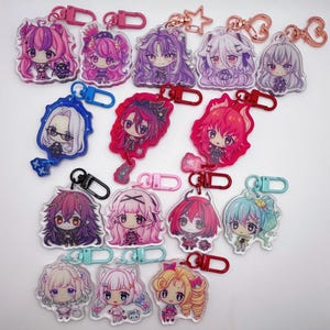 May include: A collection of fourteen acrylic keychains featuring various anime-style chibi characters with colourful hair and outfits. Each keychain is attached to a plastic or metal lobster clasp in matching colours, including pink, blue, red, and black.